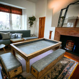 Reclaimed-wood gaming table with a recessed grey play surface and upholstered storage benches beside a fireplace.