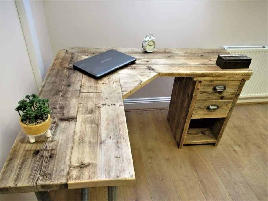 L-shaped reclaimed wood pedestal desk with drawers and a laptop.