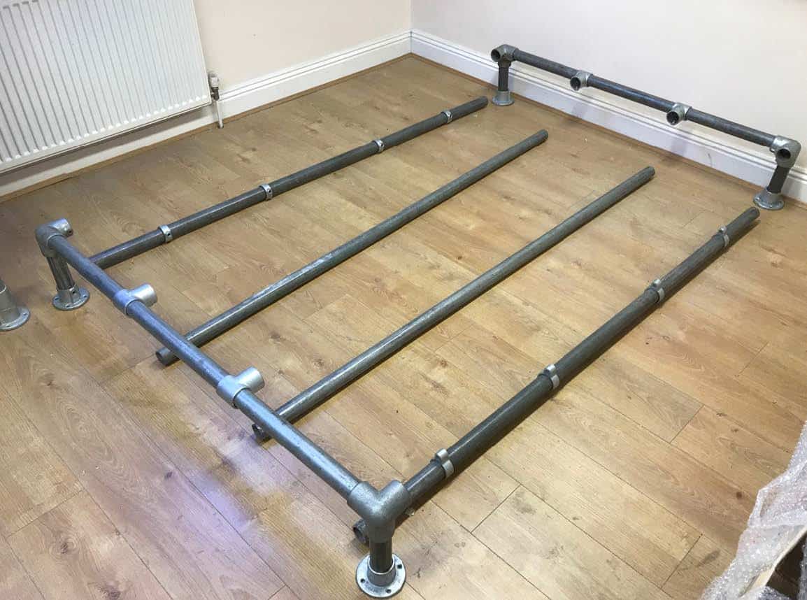 Steel pipe bed frame laid out on a wooden floor for assembly.