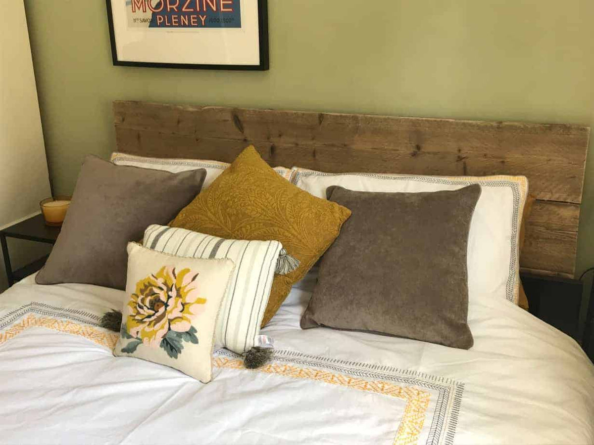 Rustic reclaimed-wood headboard behind a bed with grey, ochre and patterned cushions.