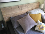 Close view of a rustic reclaimed-wood headboard above grey and ochre bed cushions.