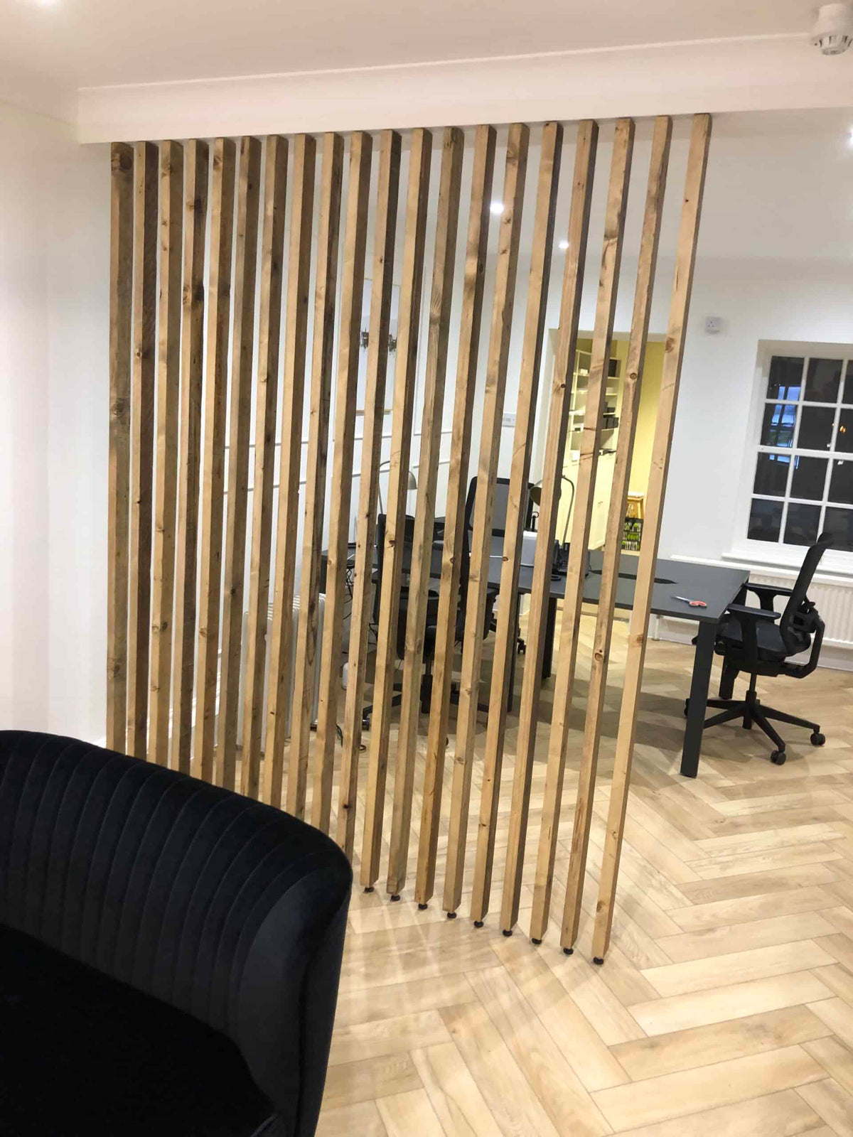 Floor-to-ceiling natural-wood slat divider separating a living area from a home office.
