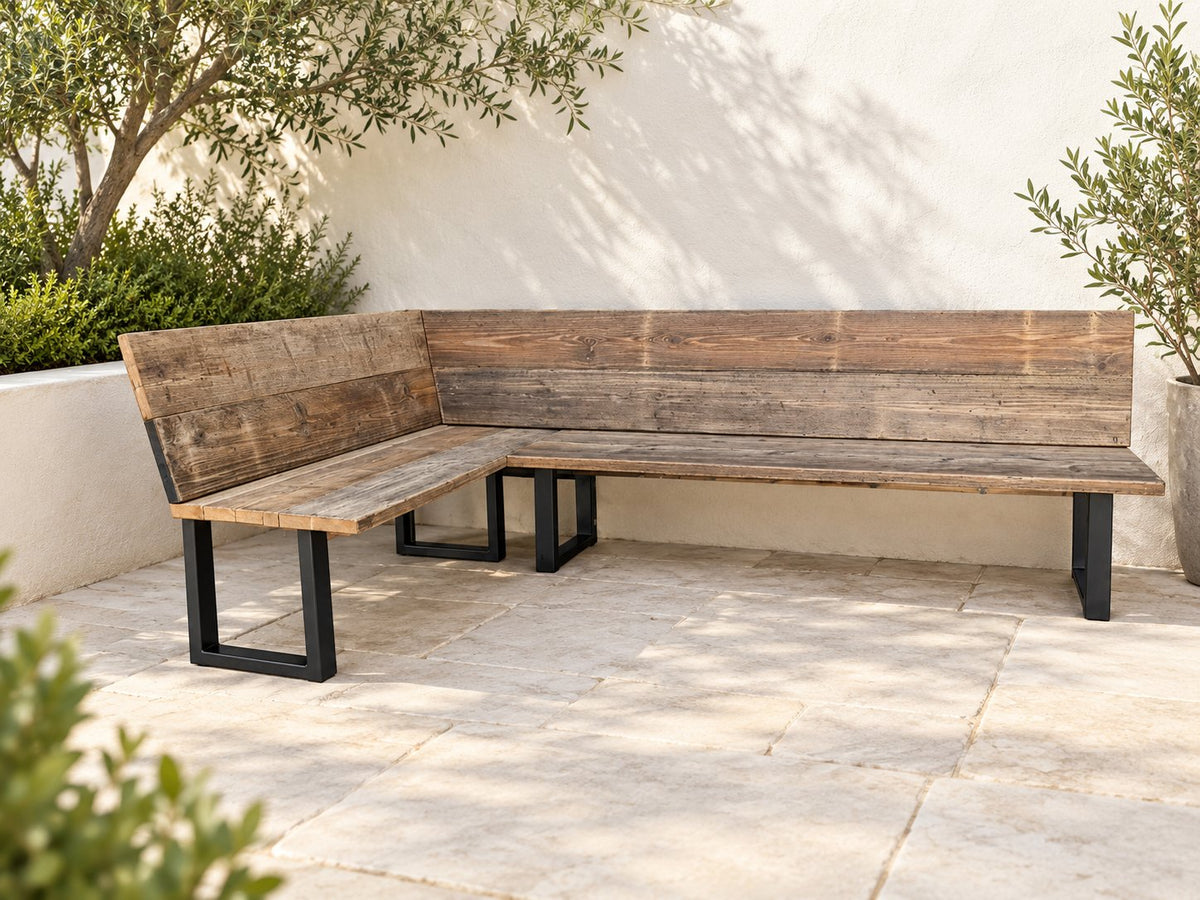 Timms L-shaped reclaimed wood corner garden bench with wooden backrests and black metal legs in a pale stone courtyard.