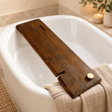 Woolston dark reclaimed wood bath caddy with a glass slot and rectangular cut-out across a white bathtub in a warm Scandinavian bathroom.